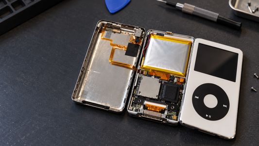 Opened iPod Classic showing its internal battery beside the white front panel on a repair bench.